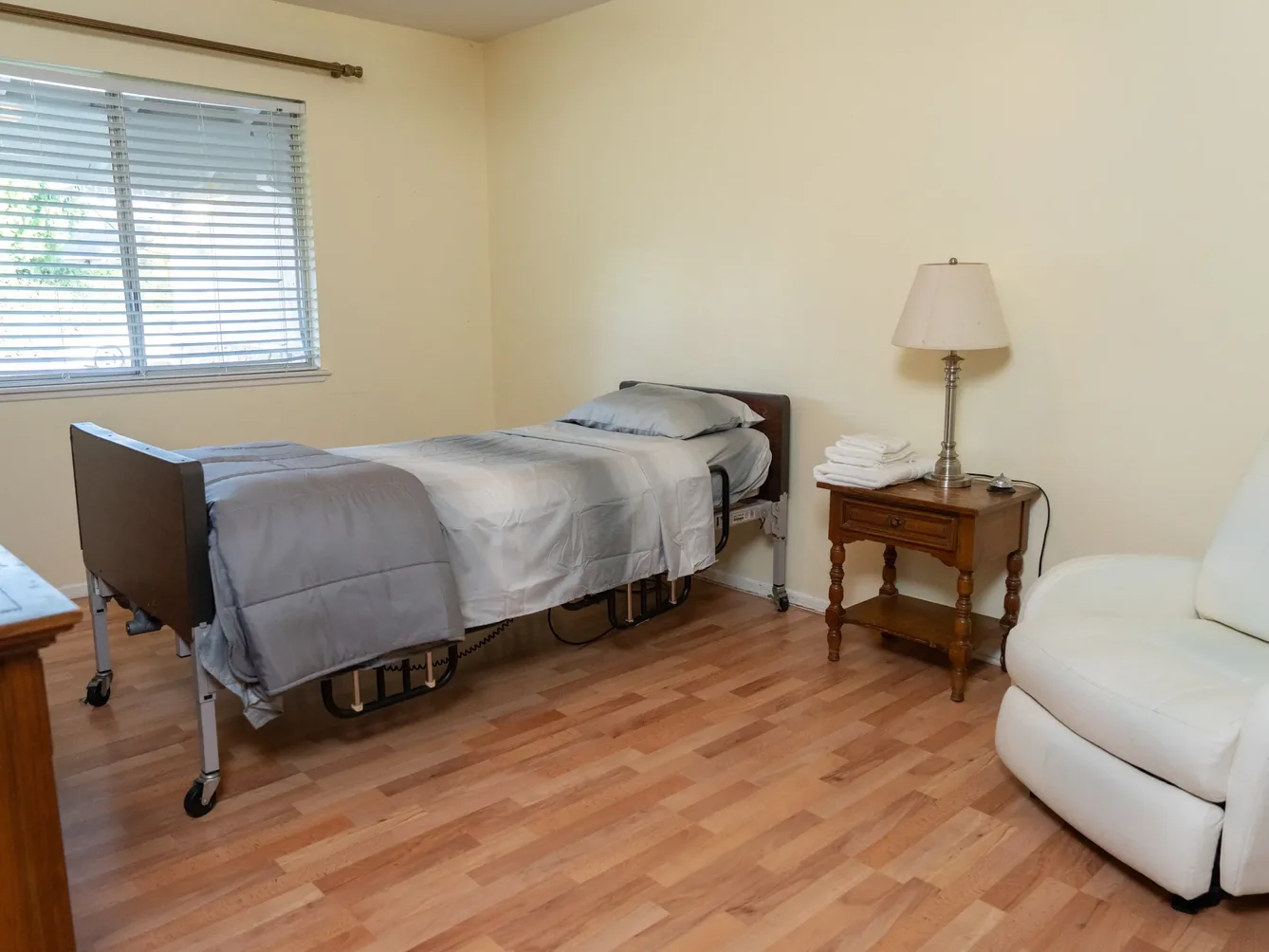 Private resident bedroom with adjustable hospital bed, accessible side table, and natural lighting.