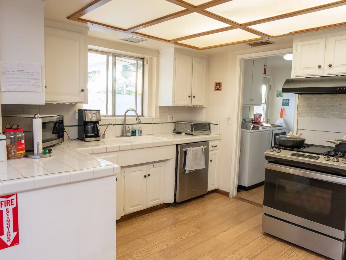 Bright kitchen with white cabinets, tile countertops, and stainless appliances in residential care home.