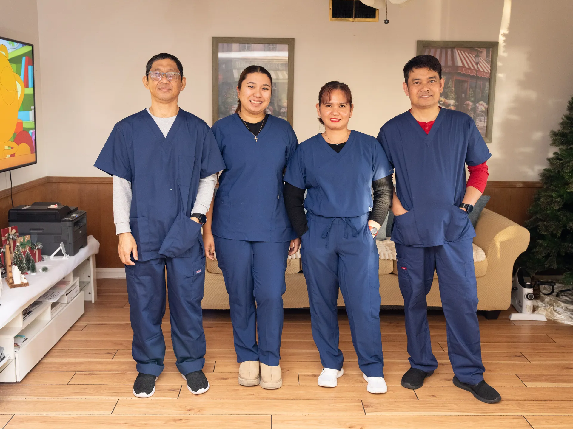 Four professional caregivers in blue scrubs posing as a team in the facility's living room.
